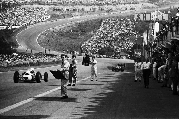 View from the pits looking down hill towards Eau Rouge, as mechanics hold pitboards to signal to drivers. View from the pits looking down hill towards Eau Rouge, as mechanics hold pitboards to signal to drivers.